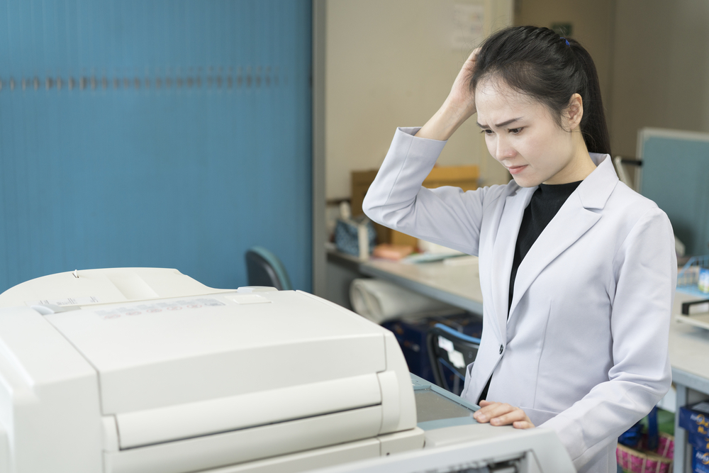 This is a photo of a lady in front of a large fax machine scratching her head.